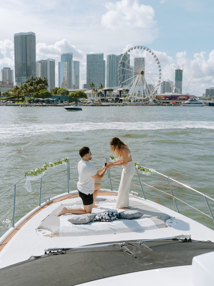 Man proposing to his partner aboard a luxury yacht in Miami with champagne and ocean views in the background.