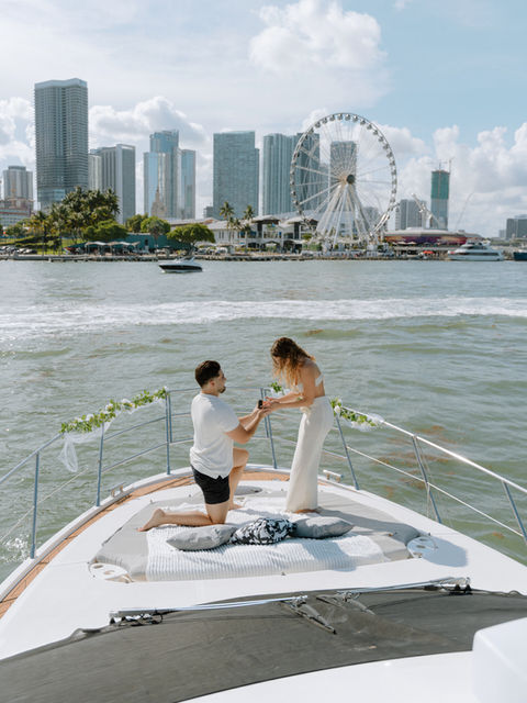Man proposing to his partner aboard a luxury yacht in Miami with champagne and ocean views in the background.
