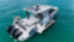 A sleek white boat with two Mercury engines floats on clear teal water. It has a spacious deck and seating area, creating a relaxed vibe.