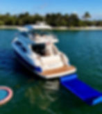 Luxury yacht Summer Girl anchored in tropical water near a palm-lined shore, with blue floating mat and calm sunny mood.