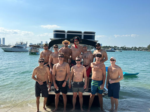 Group of bachelor party guests standing in front of their rented pontoon boat in Miami, ready for a fun day on the water.