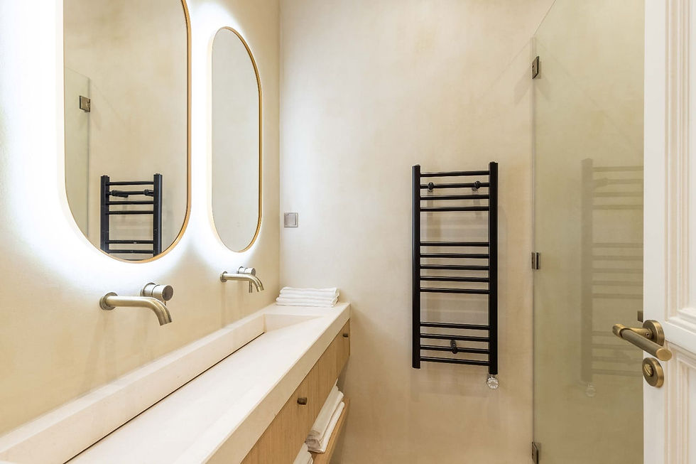 Salle de bains minimaliste avec deux miroirs ovales, lavabo blanc, porte-serviettes noir, murs beiges, ambiance calme et épurée.