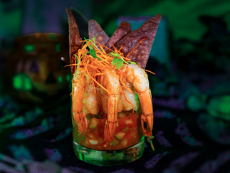 Shrimp cocktail in a glass with tomato sauce, topped with carrot shreds and cilantro, set against a dark, eerie green-lit background.