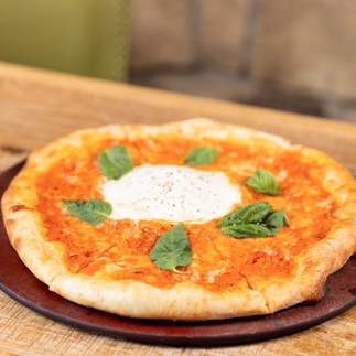 Pizza topped with burrata and basil on a wooden table. The crust is golden, and the setting is a cozy, rustic dining area.