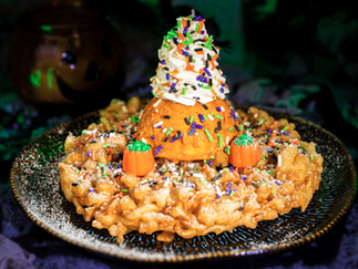Festive dessert topped with whipped cream and Halloween sprinkles sits on a plate. Includes candy pumpkins. Dark, spooky background.