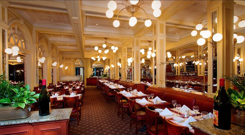 Elegant restaurant interior with empty red seats, white tablecloths, and glowing chandeliers. Large wine bottle and plants adorn the foreground. A new breakfast buffet option will be offered at Chefs De France. This limited time offer will be available of Fridays and Saturdays during the festival.