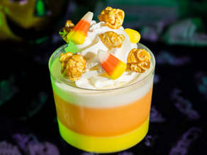 Candy corn parfait with whipped cream, caramel popcorn, and candy corn topping. Halloween-themed background with green glow.