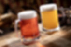 Two frothy beer mugs on a wooden table; one amber, one pale yellow. Warm, blurred background creates a cozy ambiance.