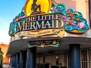 Vibrant entrance sign for “Tiana’s Bayou Adventure” decorated with colorful flowers, leaves, and intricate patterns, with the text displayed in bold, playful lettering against a rustic wooden background.