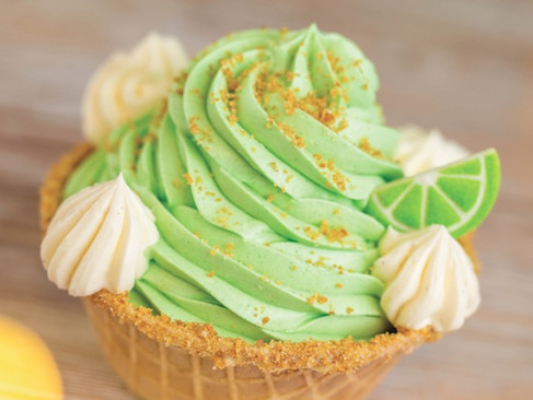 Green swirl cupcake with lime wedge and cream dollops on wooden surface. Bright, colorful dessert evokes a fresh, cheerful vibe.