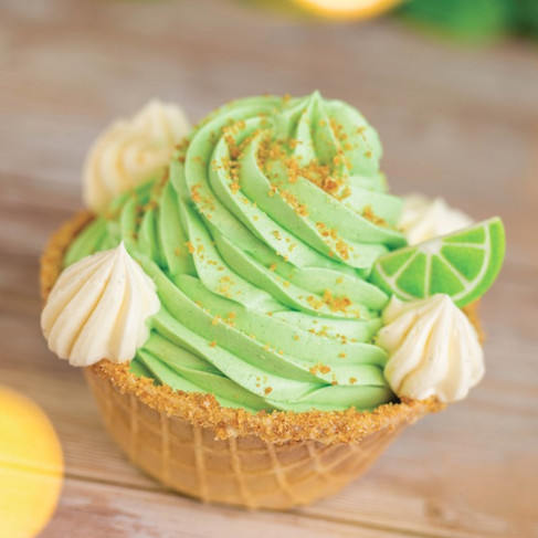 Green cupcake swirls in waffle cup, topped with lime slices and cream dollops, on wooden table. Bright and fresh mood.