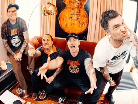Four tattooed men pose playfully in a room with a red sofa, orange guitar art, and striped rug. Two wear black shirts, one a plaid shirt, and one a white tee. New Found Glory was just added to the Eat to the Beat concert series at EPCOT.