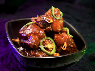 Close-up of glazed meat chunks with green bell pepper slices in a black bowl. Background is dark with a purple and green hue.