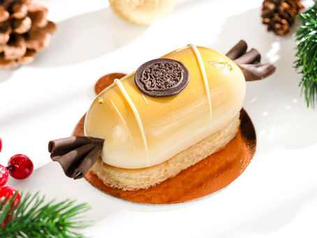 A cake resembling a wrapped candy with chocolate curls sits on a golden base. Surrounded by pinecones and red berries, creating a festive feel.