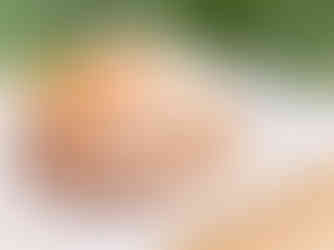 Sugary pastry with whipped cream and a mandarin slice on top, set on a white tray on a wooden table, with a blurred green background.