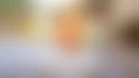 Three colorful swirled ice creams in martini glasses on a wooden table, garnished with pineapple, sprinkles, and berries, outdoors.