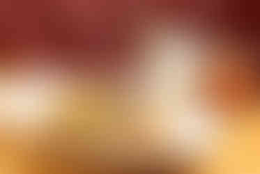 Plate of grilled fish with vegetables on a wooden table. Two cocktails behind on a red cushioned booth. Warm and inviting atmosphere.