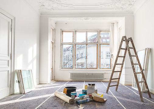Bright room under renovation with a ladder, paint supplies, and large windows