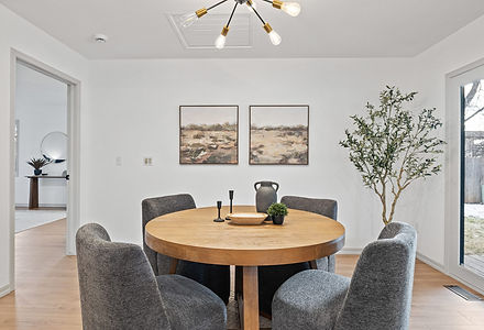 Dining area with a round wood table, four gray upholstered chairs, two landscape paintings and a potted olive tree, Narrative Interiors home staging serving Windsor, CO