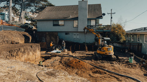 a construction site with a yellow cat excavator in front of a house