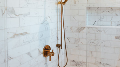 a shower with marble tiles and a brass shower head