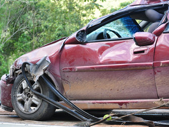A red car has a crumpled and torn front bumper, dents on the side, and a cracked windshield.