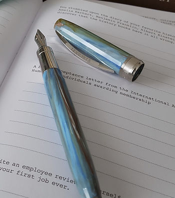 A marbled blue Visconti fountain pen is uncapped and laying on a workbook with black text and lines printed on white paper.