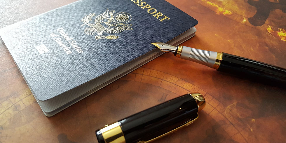 Photo: A US passport and an uncapped fountain pen on a wooden table top. The body of the fountain pen is black and the hardware is shiny gold. The section and nib are silver with gold accents.