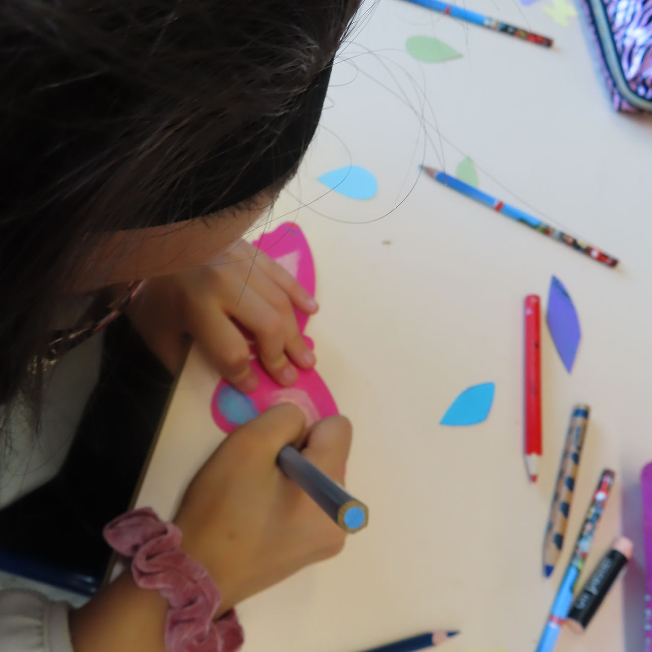 Enfant dessine un papillon rose sur papier avec des crayons, création artistique colorée.