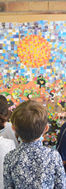Enfants regardant une grande mosaïque colorée représentant un soleil et paysage.