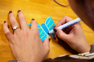 Une personne écrit sur un papillon bleu avec un marqueur blanc GIOTTO.