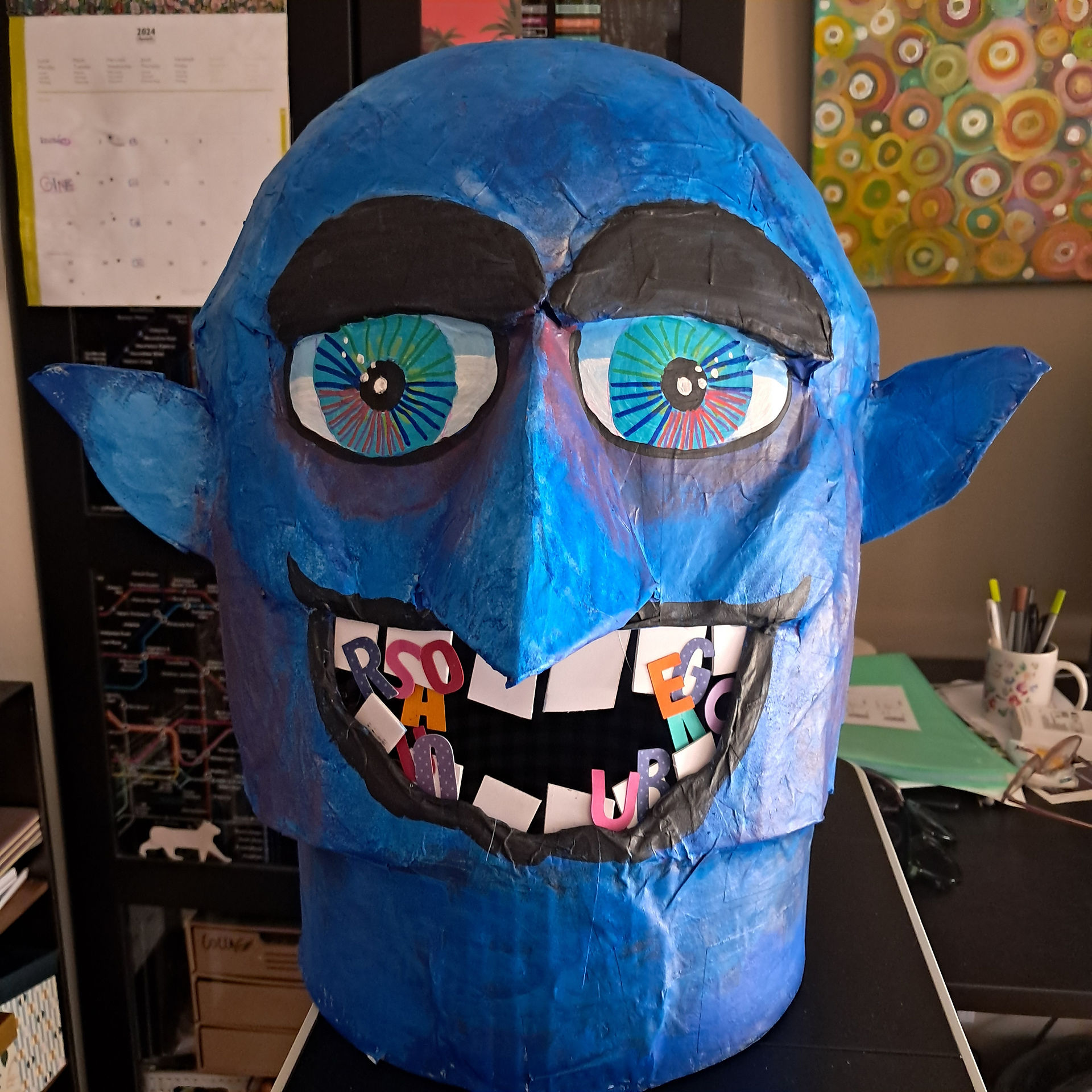 Un grand visage bleu souriant avec des yeux brillants et des lettres colorées à l'intérieur.