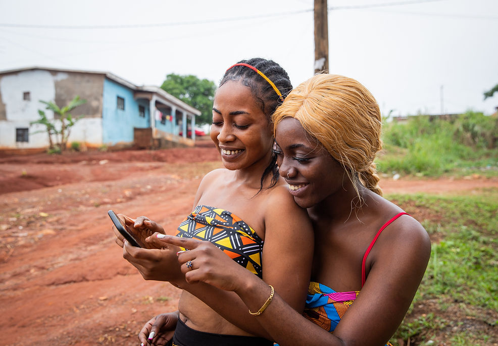 Two young african women looking into one phone and smiling at what they are seeing.