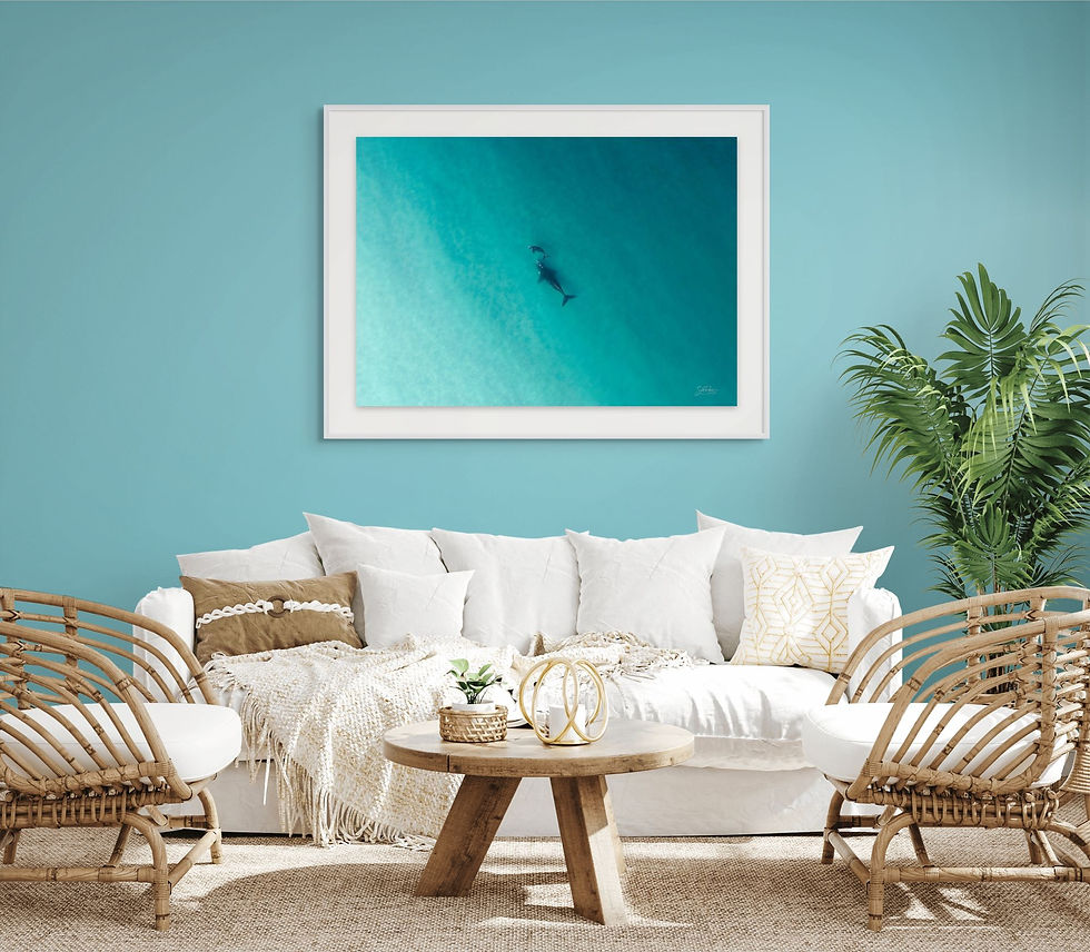 Framed ocean photography print displayed above a coastal-style sofa in a bright, beach-inspired living room.