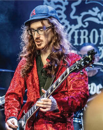 Marty Alocco in a red shirt and blue Astros baseball cap playing AC/DC music on his guitar at an Appetite for Voltage concert