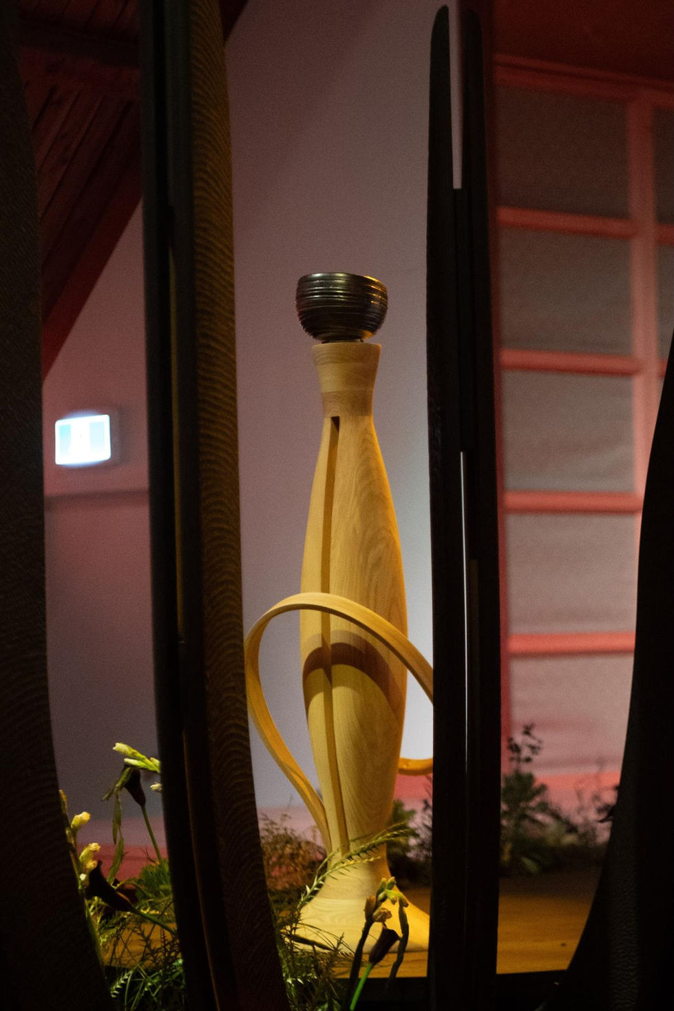 Wooden sculpture with a dark top, surrounded by plants.