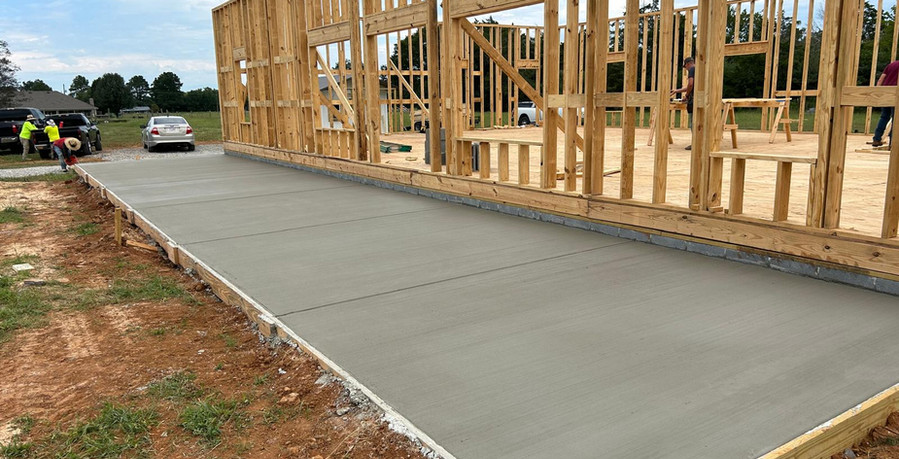 Newly poured concrete driveway beside house framing during construction
