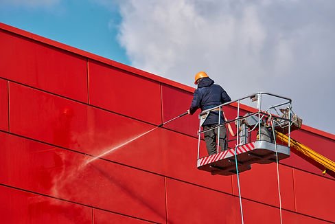 Worker wearing safety harness washes wall facade at height on modern building in a crane..