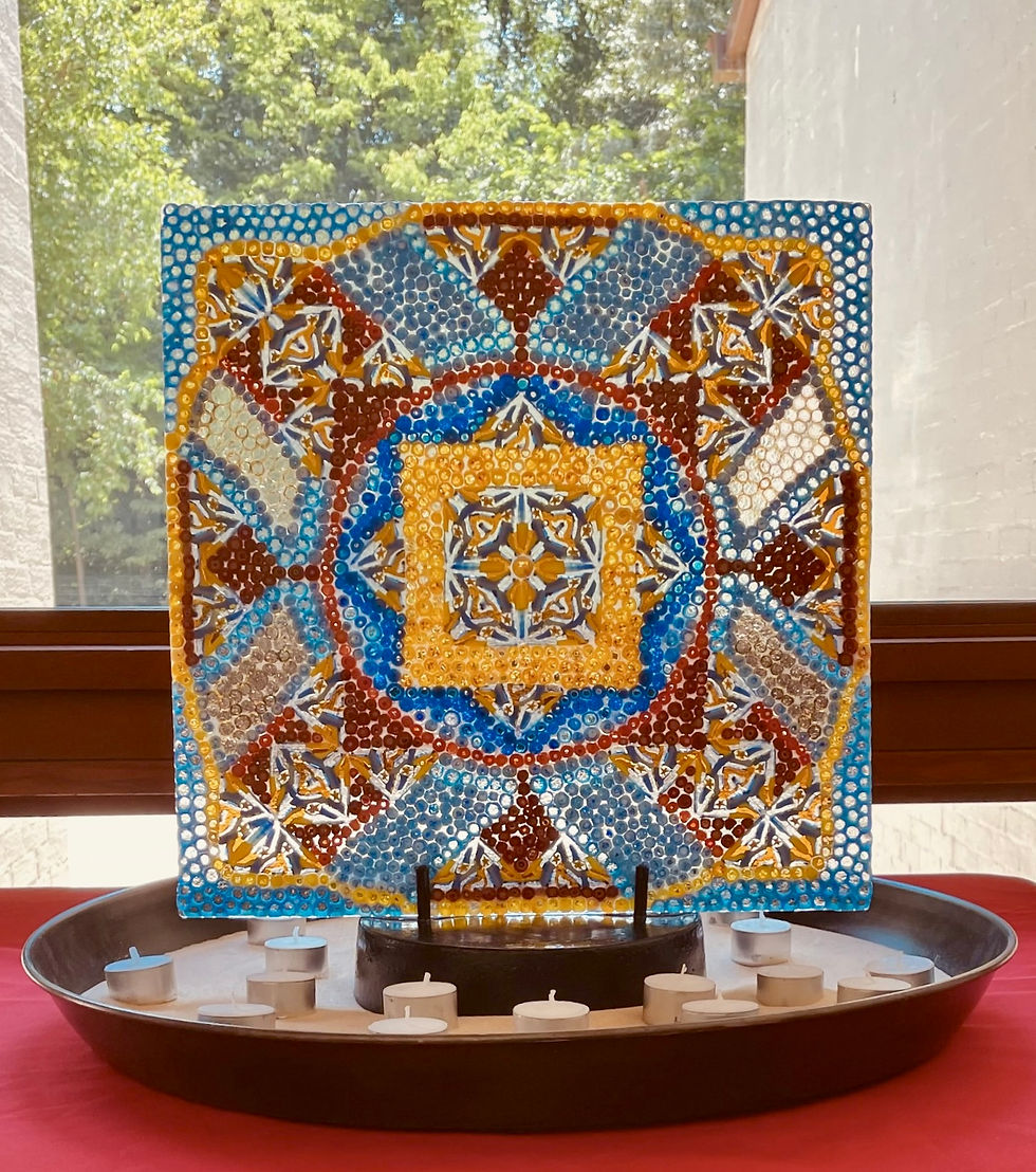 A colorful glass mandala set in sand and surrounded by candles.