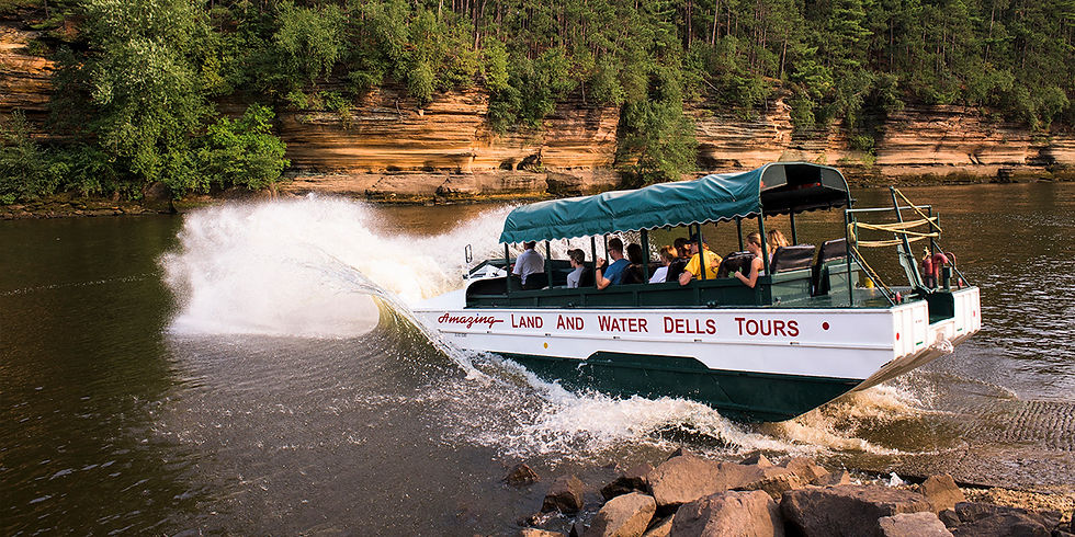 Tour boat labeled Amazing Land and Water Dells Tours splashes across a river beside wooded sandstone cliffs.