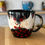 Thumbnail: Artistic floral design on a black coffee mug with red flowers and ChernyArtStudio.