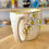 Thumbnail: White ceramic mug with yellow and black floral design, ChernyArtStudio.