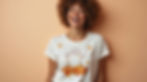 Smiling woman with curly hair wearing a white print-on-demand T-shirt featuring a cheerful ghost and autumn leaves. Peach background. Bright and joyful mood.