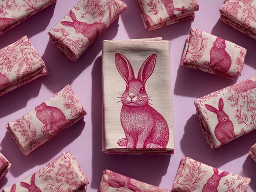 Folded pink napkins with rabbit prints on a purple background. Central napkin displays a detailed rabbit image, creating a playful pattern.