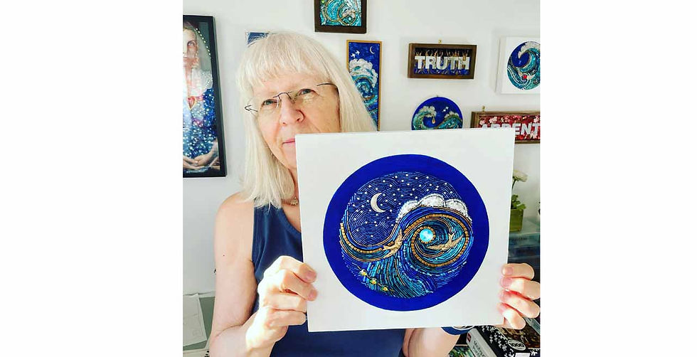 Diana Maus of Mosaic Moods on Etsy in glasses holds blue circular artwork in a bright studio; wall signs read TRUTH and EVENT. She's celebrating her successful business as a woman over 40.