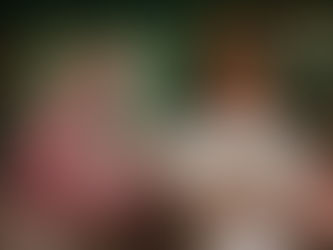 Woman with red hair in a white dress stands confidently in an art studio. A pink giraffe painting and paintbrushes are in the background.