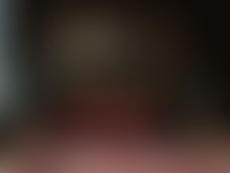 Elegant room with dark walls features a large painting of a cloaked figure in a misty forest. Red sofa, ornate rug, plants, and lamp. Cozy mood.