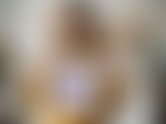 Smiling woman in a yellow sweater holds a framed picture of a purple koala. Art supplies and colorful drawings fill the bright room.