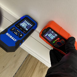 Moisture meter reading high levels on wall baseboard — water intrusion detection by Rock Bottom Restoration technician.