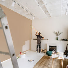 Living room restoration in progress with drywall, drop cloths, and scaffolding — ceiling and wall repairs after water or fire damage.